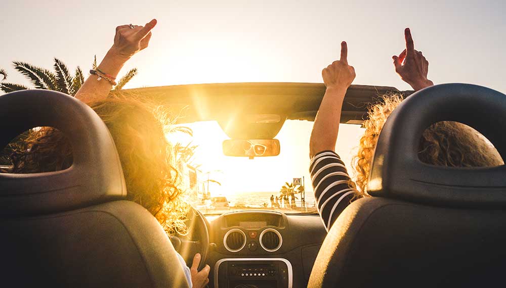 2 friends driving with their hands up
